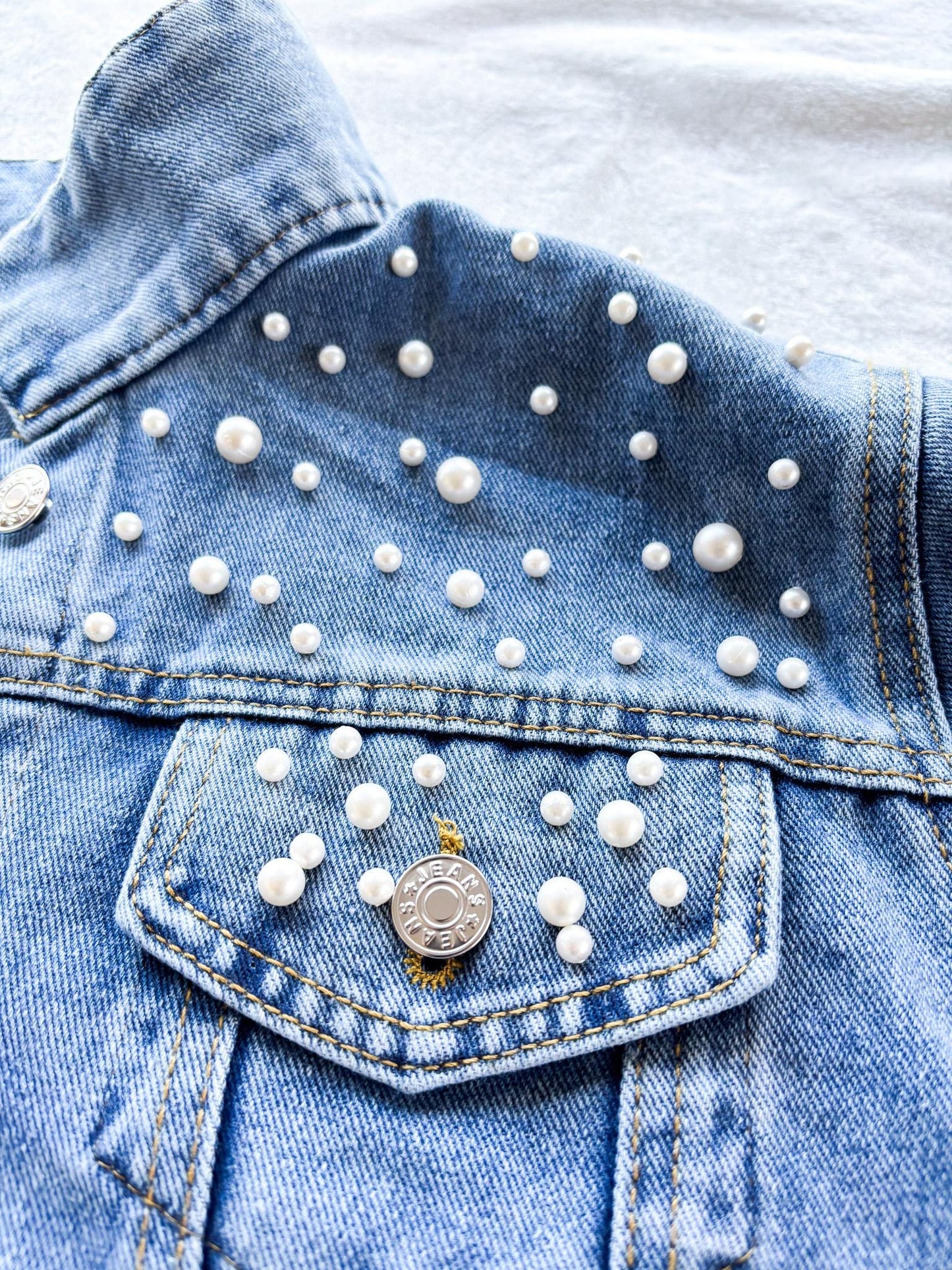 a denim jacket with white pearls on it