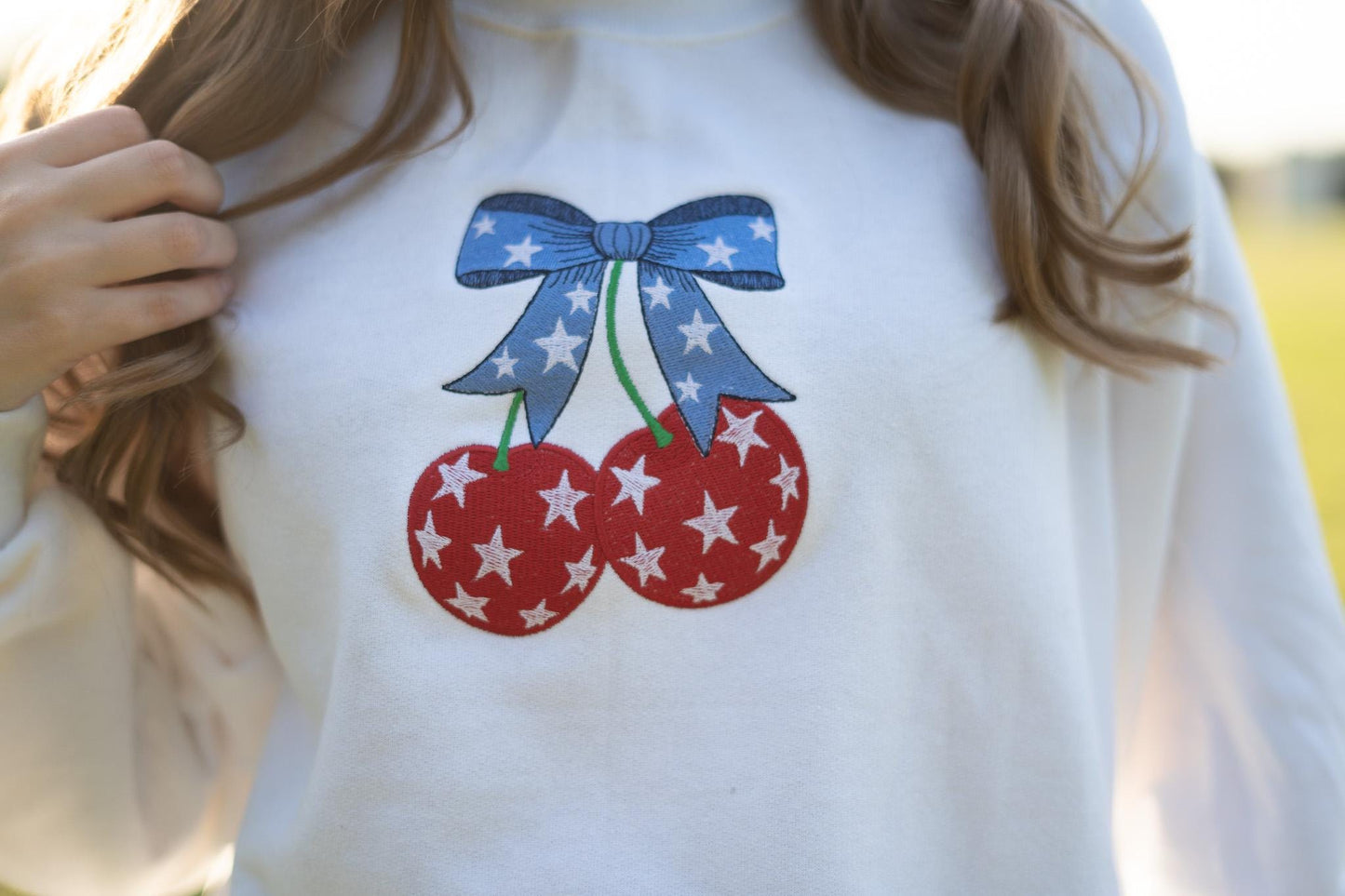 a woman wearing a white sweatshirt with red, white and blue cherries on it