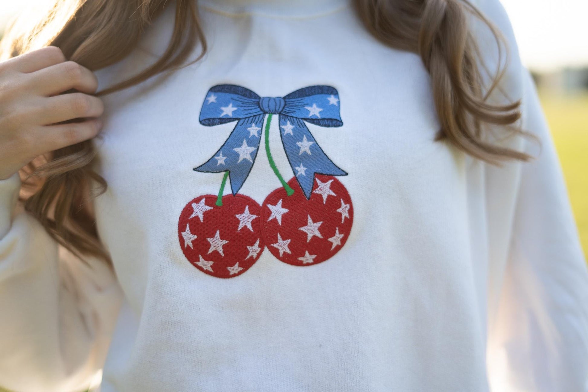 a woman wearing a white sweatshirt with red, white and blue cherries on it
