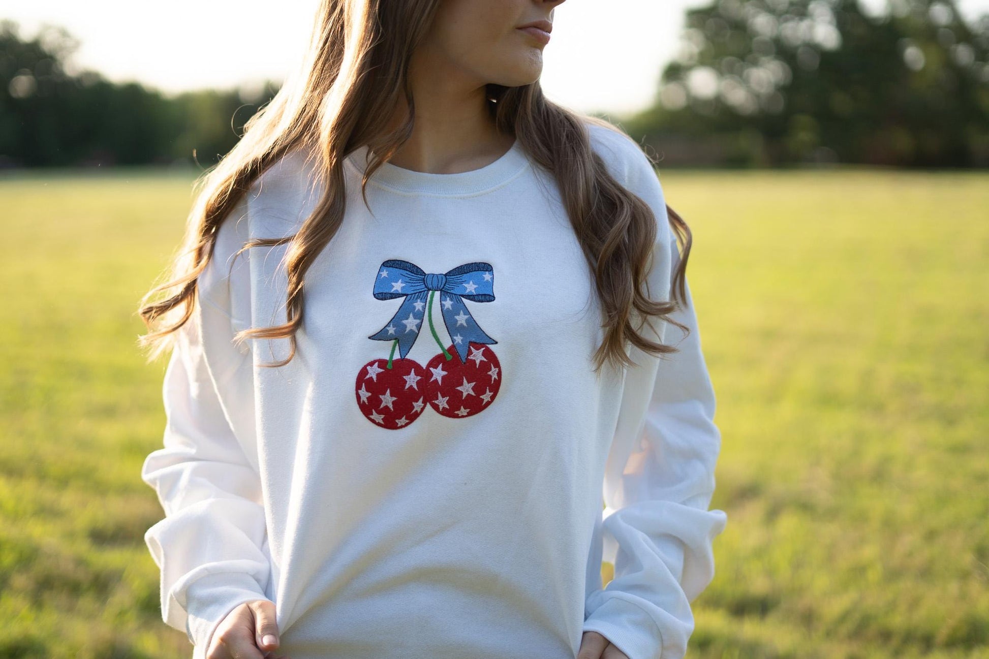 a woman standing in a field wearing a sweatshirt with cherries on it
