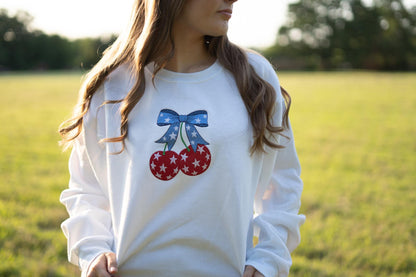 a woman standing in a field wearing a sweatshirt with cherries on it