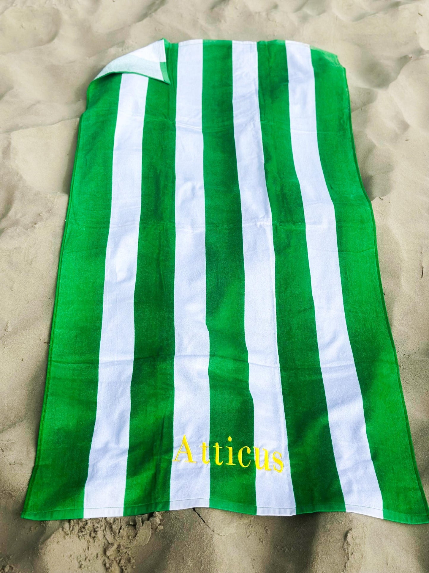 a green and white towel laying on top of a sandy beach